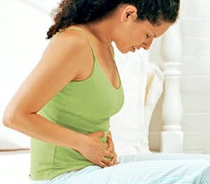 woman with menstrual cramps sitting on bed holding her abdomen