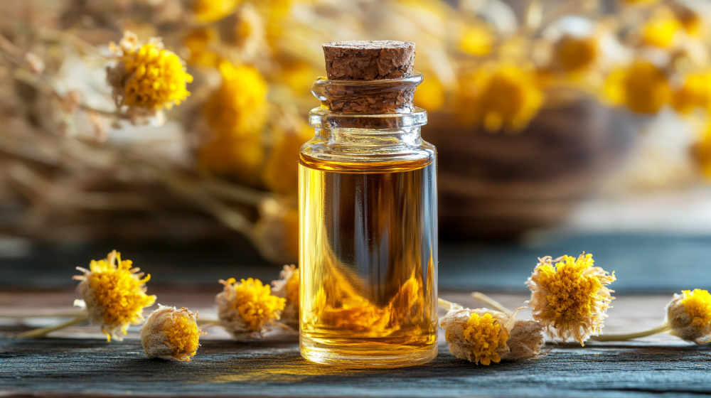Glass bottle of essential oil with yellow flowers.